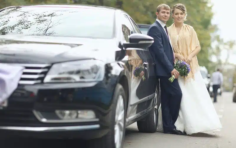 Bride and groom beside a wedding transfer vehicle